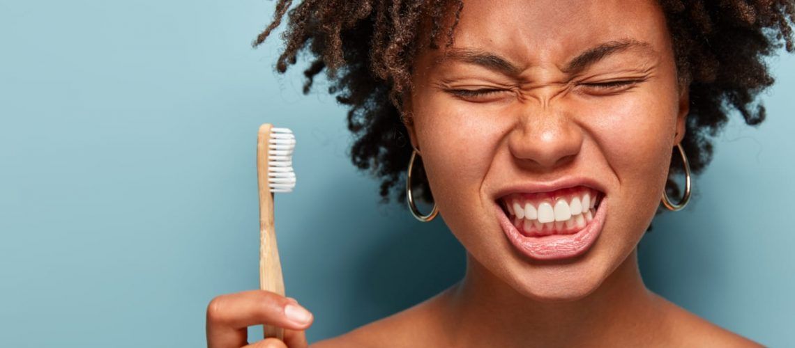 Woman with toothbrush making pained face