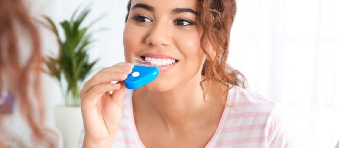Young African-American woman using teeth whitening device at home