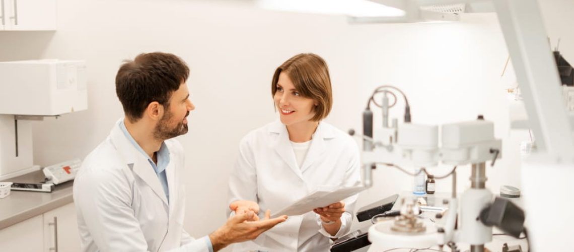 Two dental technicians are discussing a document next to modern milling machine
